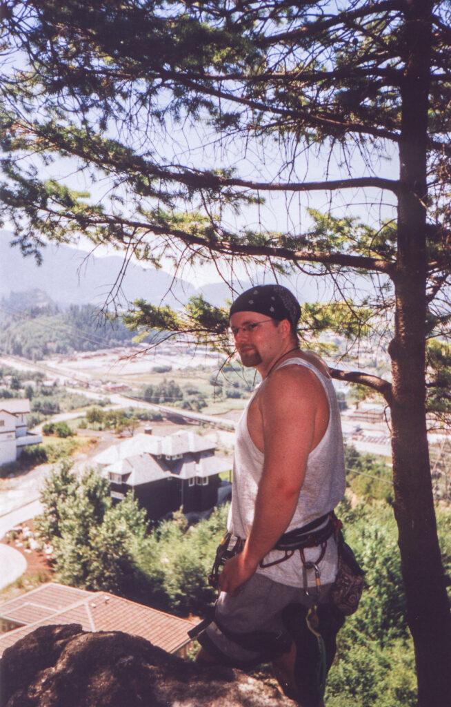 Me standing on top of the bluffs in squamish with a climbing harness on and climbing gear.